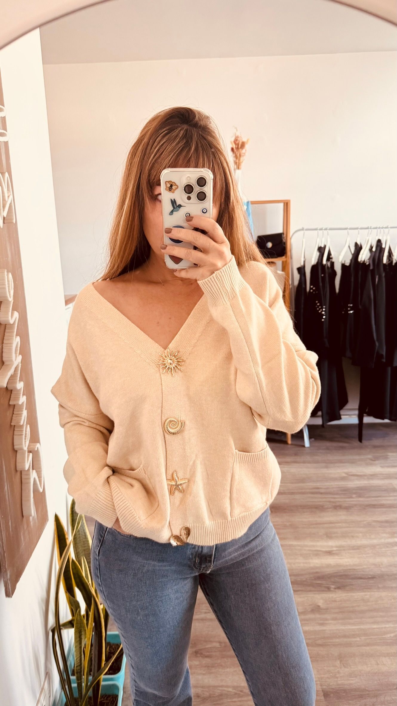 Una persona se toma una selfie frente al espejo con una blusa beige y jeans azules en una tienda de ropa.