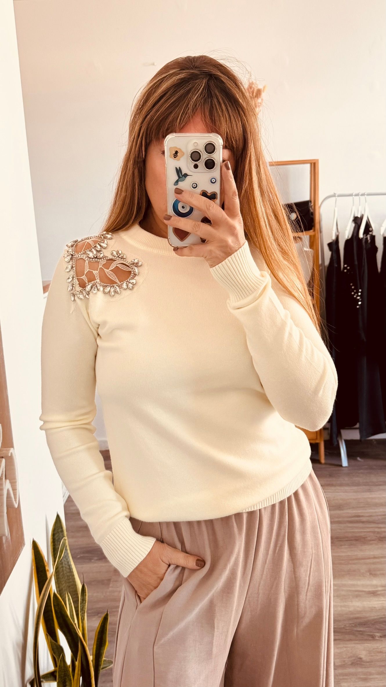Una persona se toma una selfie frente al espejo con un suéter color crema y pantalones color rosa pálido en un vestidor.