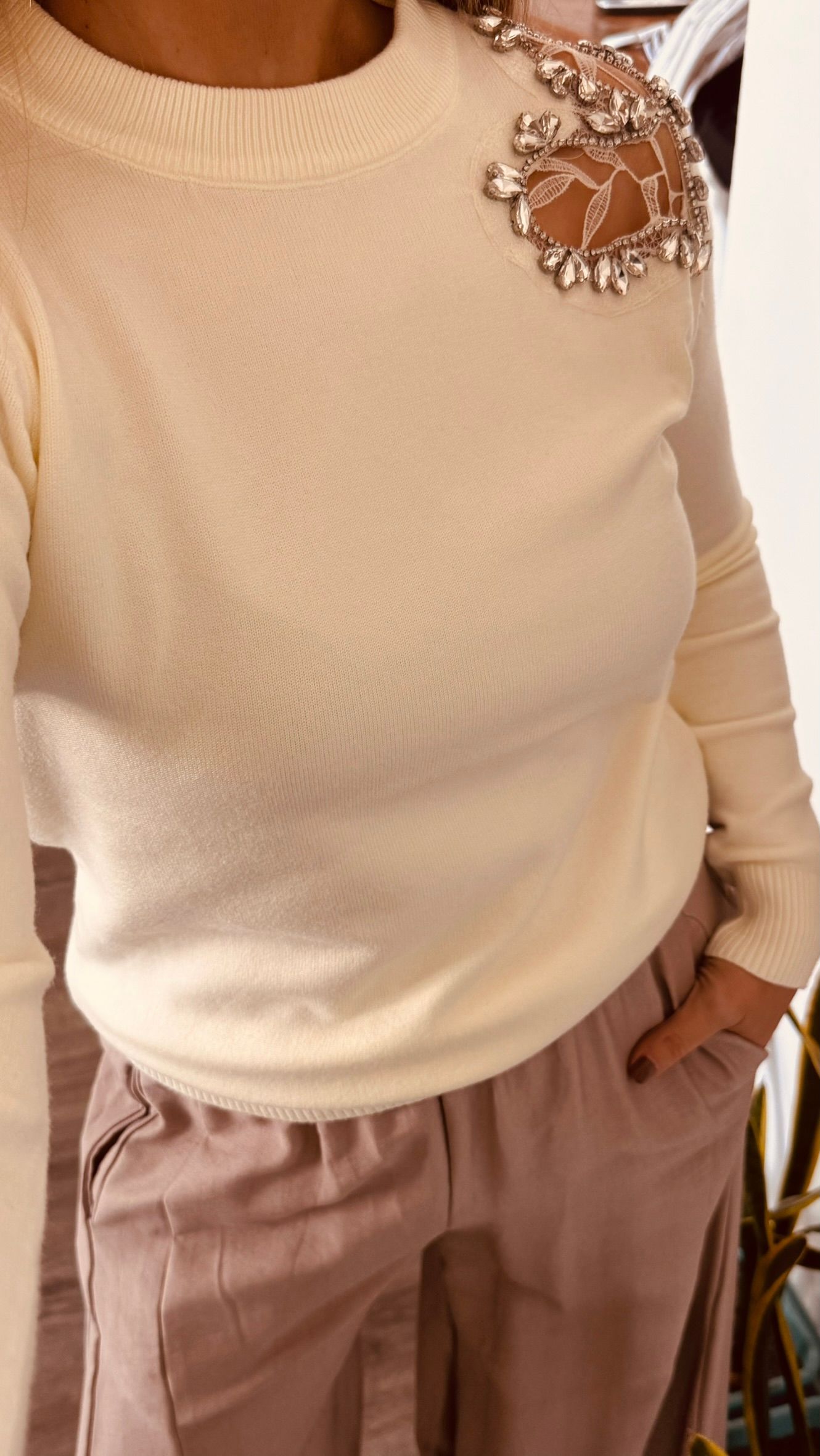Una persona se toma una selfie frente al espejo con un suéter color crema y pantalones color rosa pálido en un vestidor.
