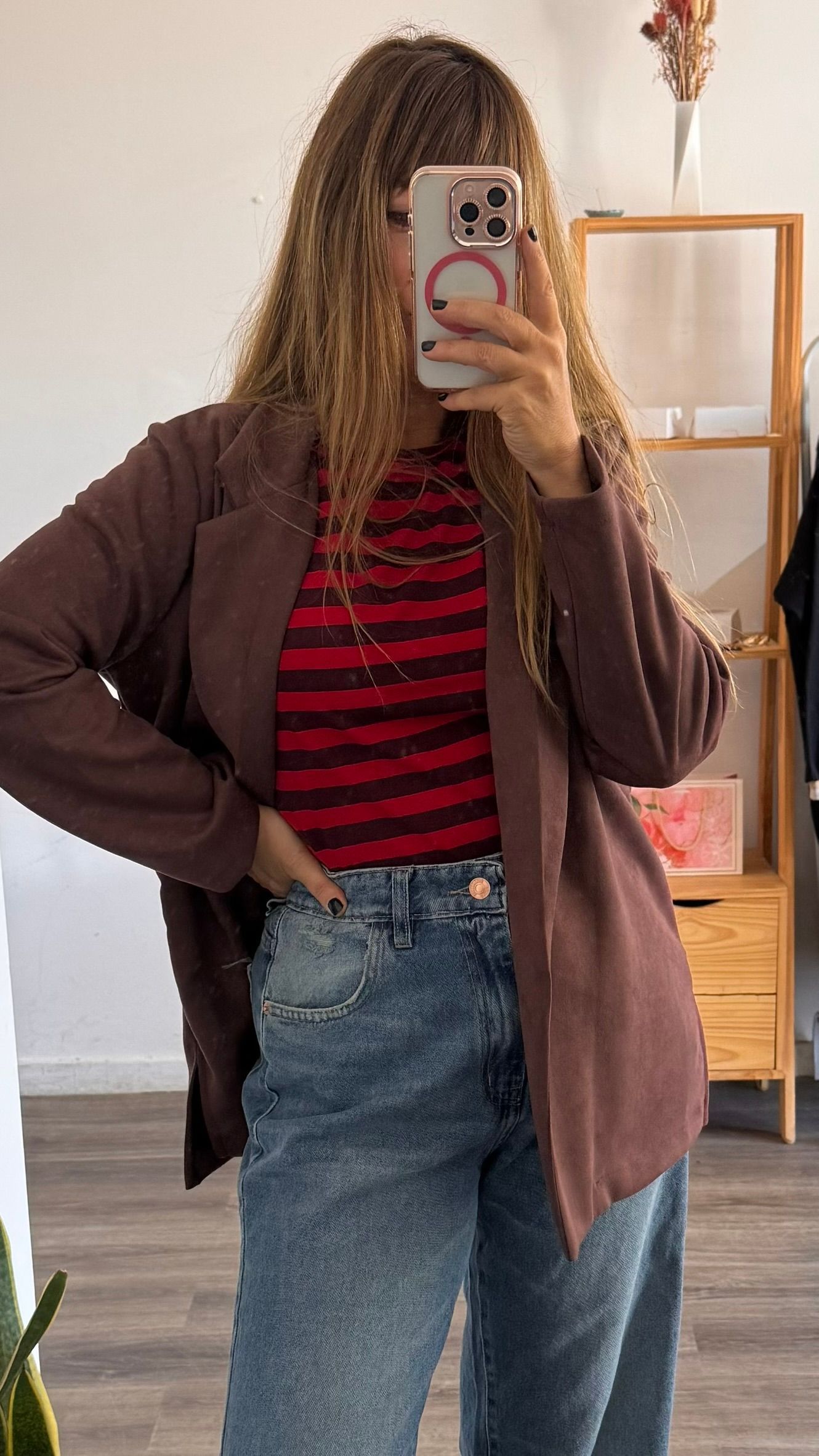 Persona con camisa de rayas rojas y negras, chaqueta marrón y pantalones vaqueros azules, de pie en el interior de un edificio.