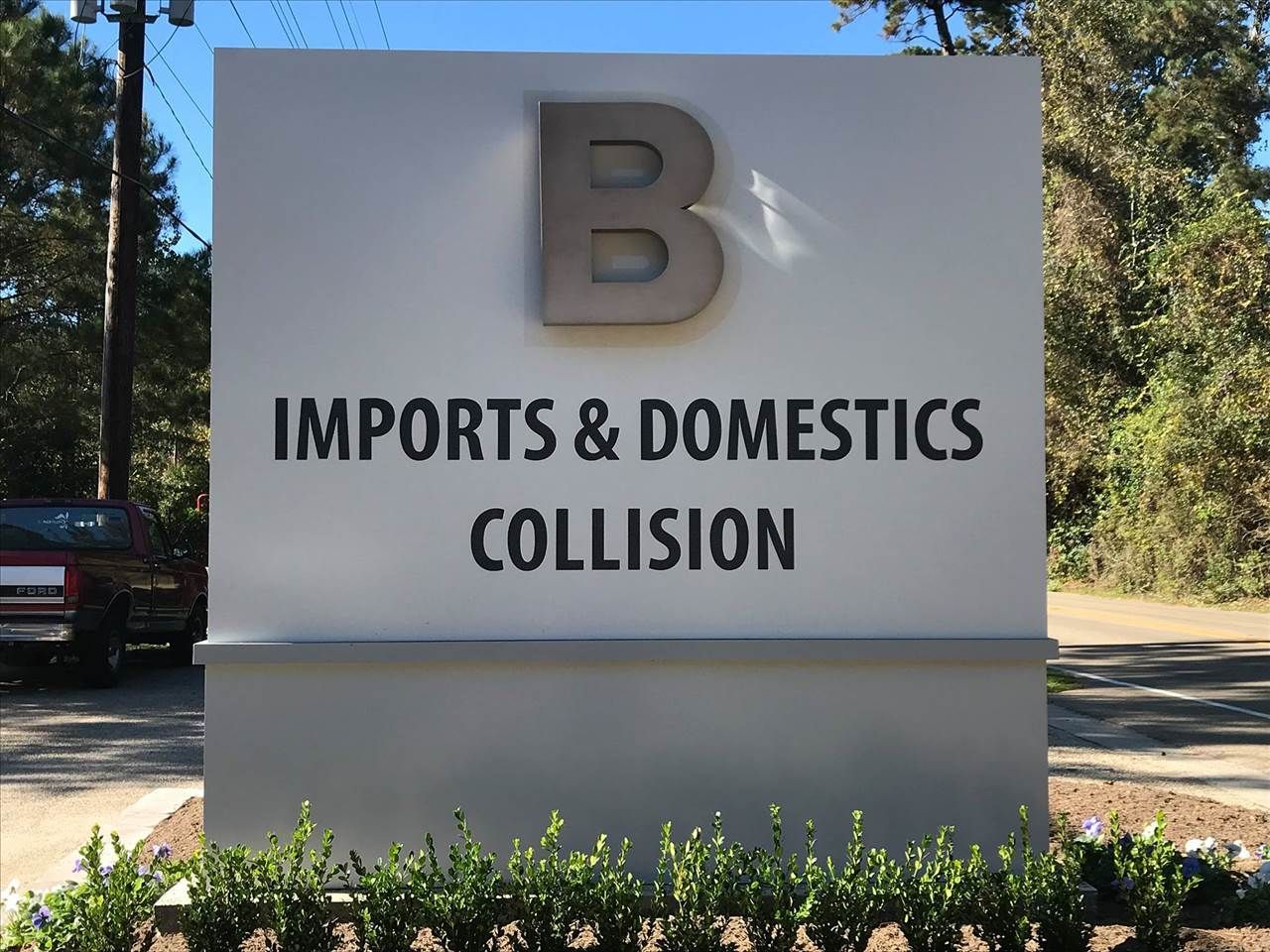 Sign for B Imports & Domestics Collision on a gray roadside monument sign