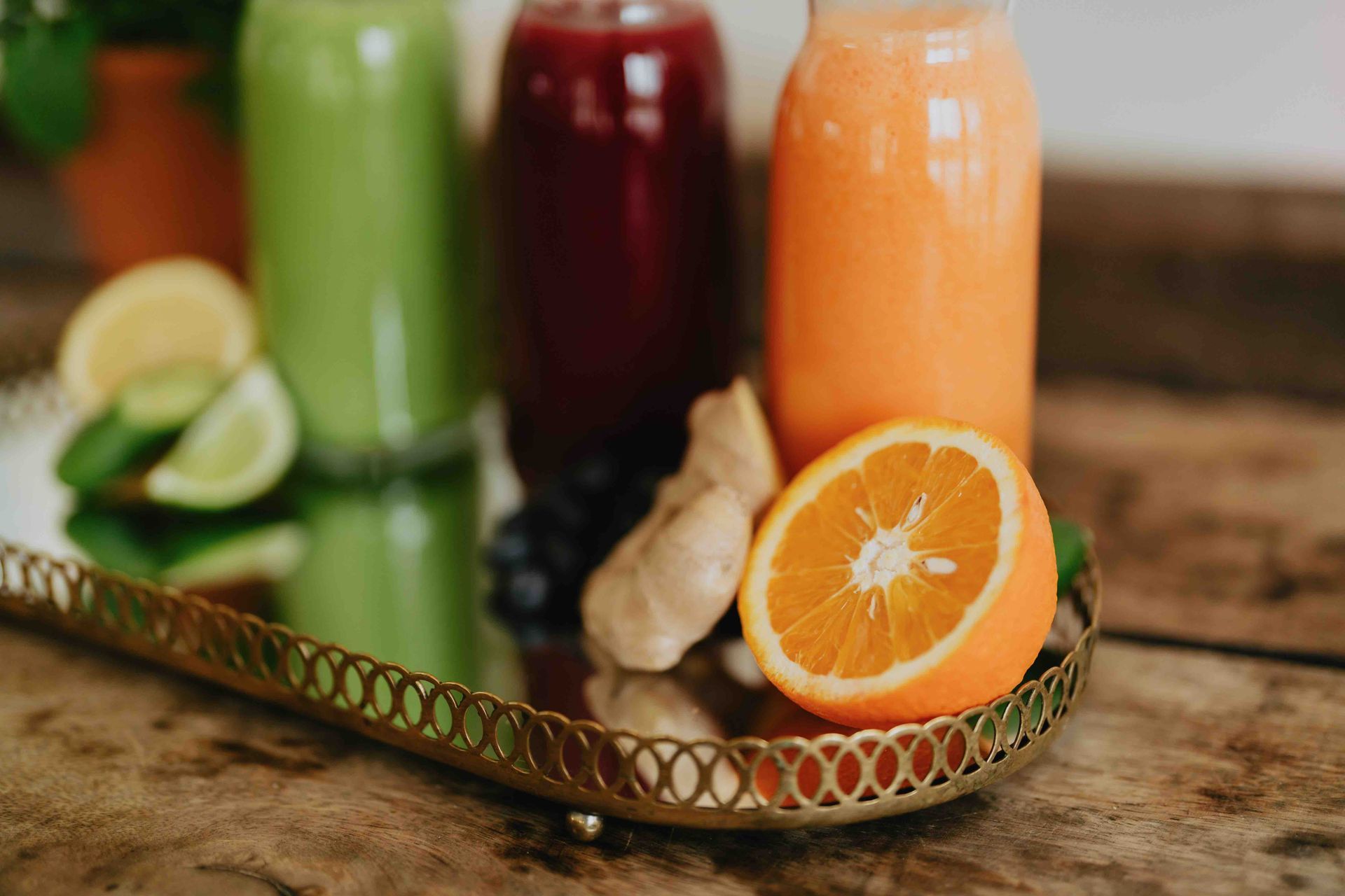 A tray with juices , oranges , lemons and ginger on a wooden table.