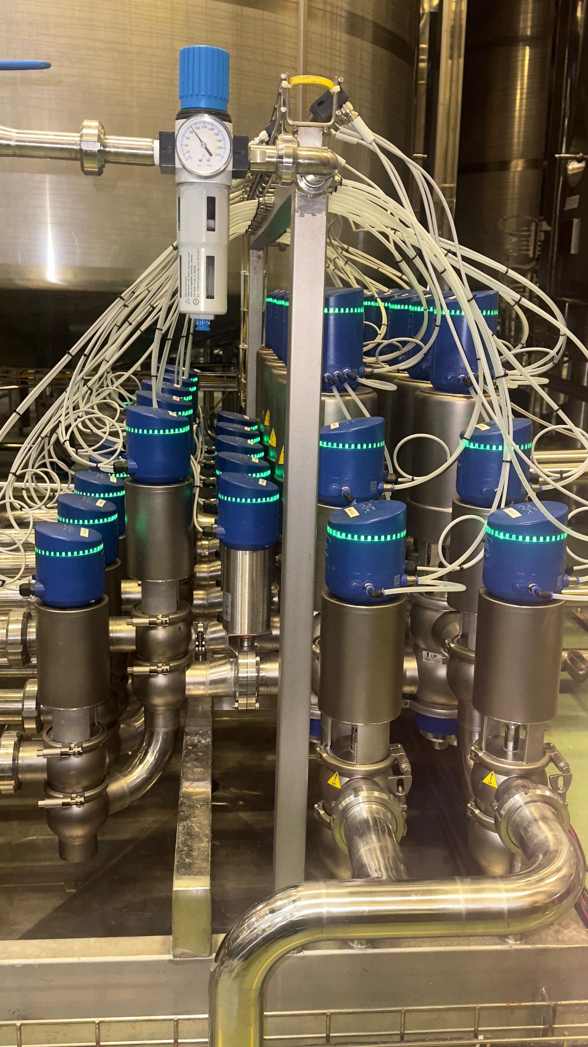 Válvulas industriais em aço inoxidável com atuadores pneumáticos e tubulação na cor azul.