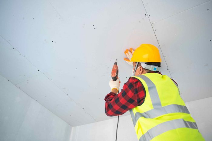 A construction worker is using a drill to fix a ceiling.