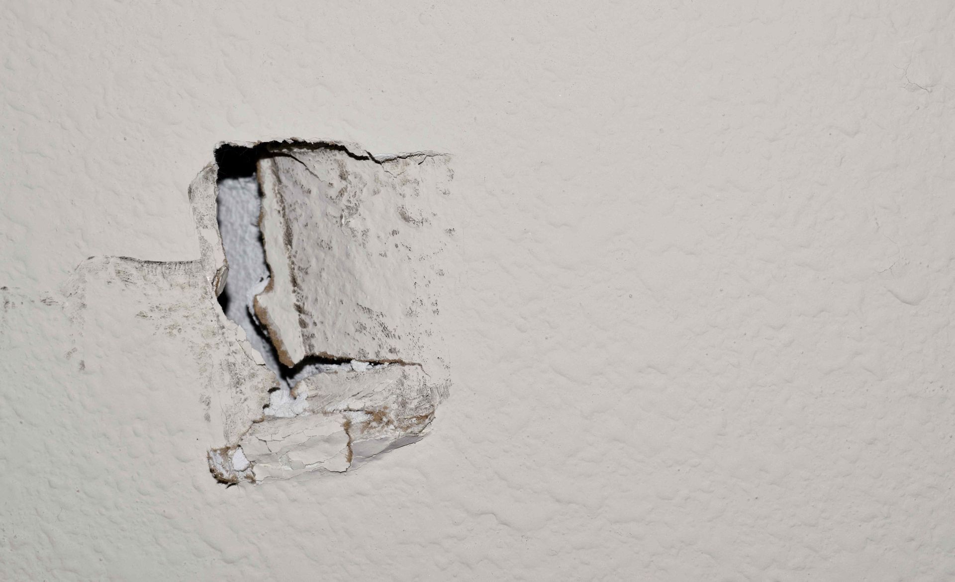 A hole in a white wall with a piece of concrete sticking out of it.