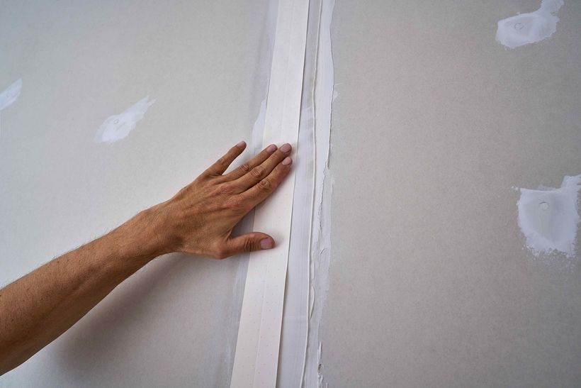 A person is touching a drywall corner with their hand.