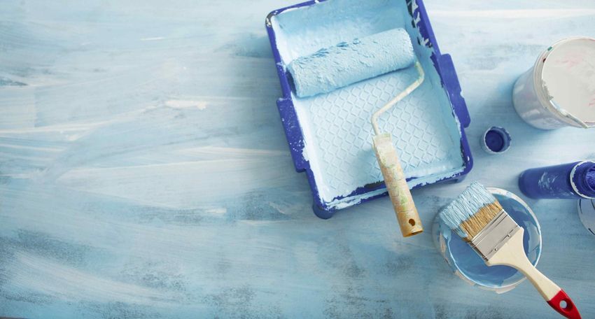 A paint roller and brush are on a blue table.