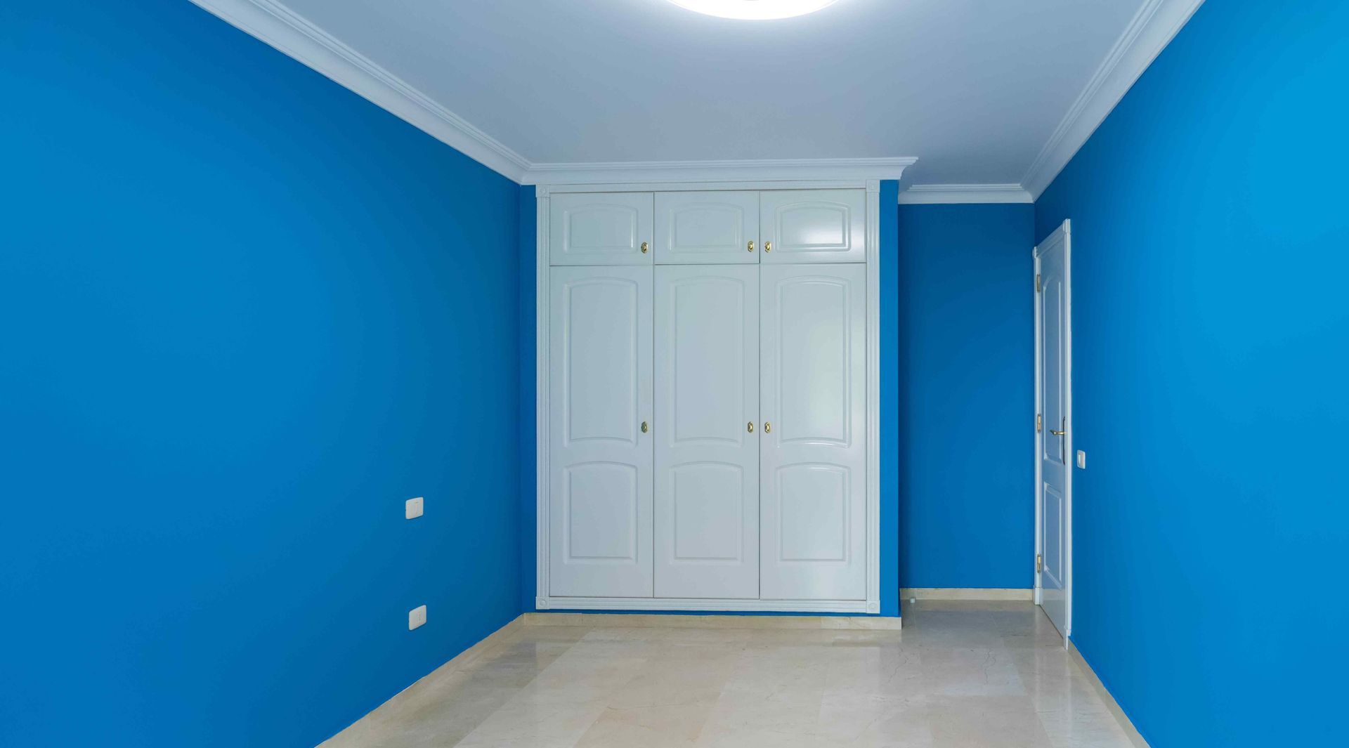 An empty room with blue walls and white cabinets.