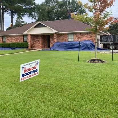 A residential home with a new roof, Bohon Roofing sign in yard, blue tarps, and a dump truck.
