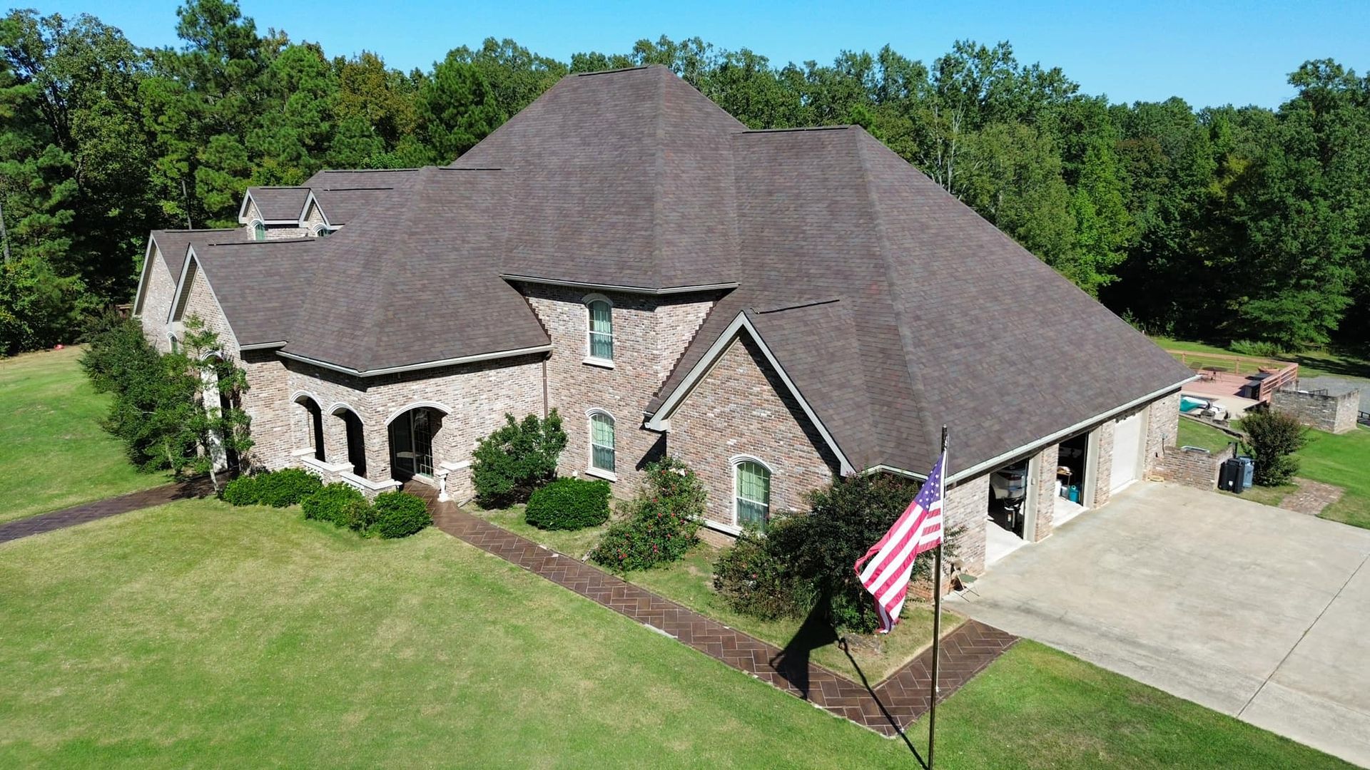 Brick house with brown roof, green lawn, and American flag in front.