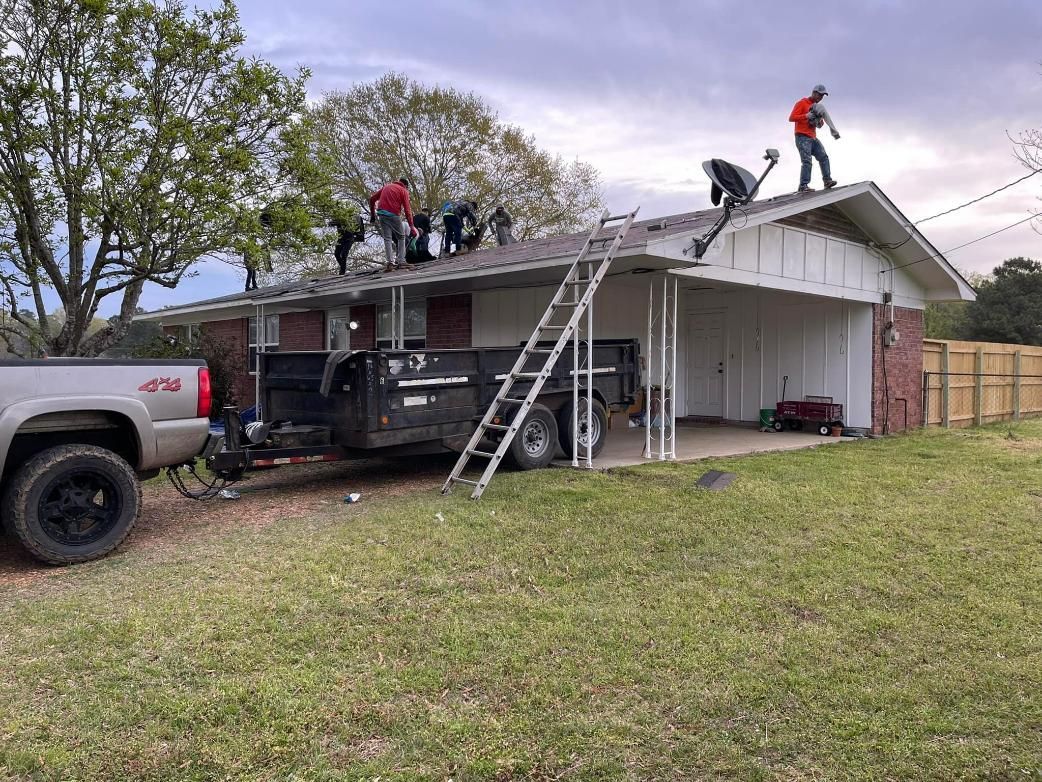Roofers working on a residential house roof, dump truck and ladder present.