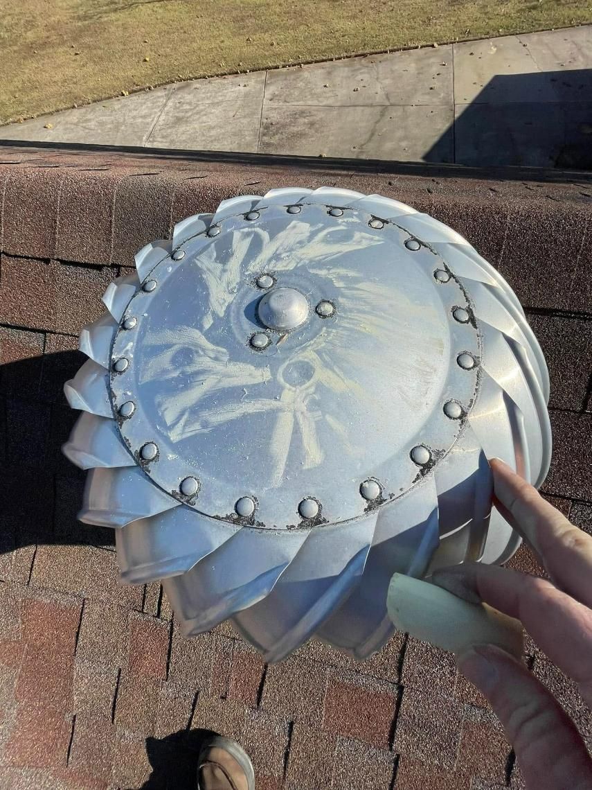 Silver roof turbine vent on a brick roof, hand holding a piece, sunny day.