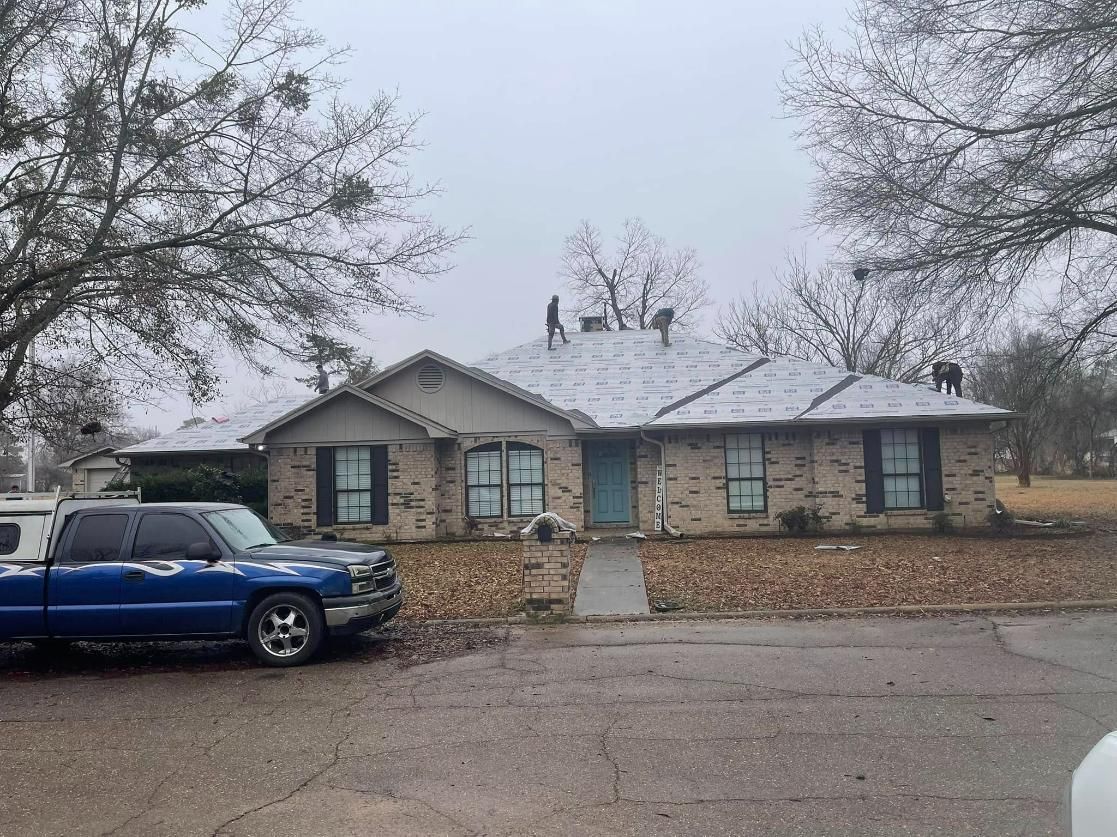 A brick house with snow-covered roof, blue truck parked in front. Overcast day.