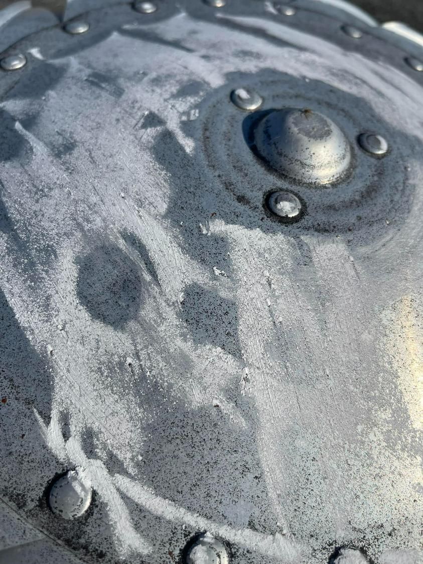 Close-up of weathered, riveted metal surface with a raised central dome.