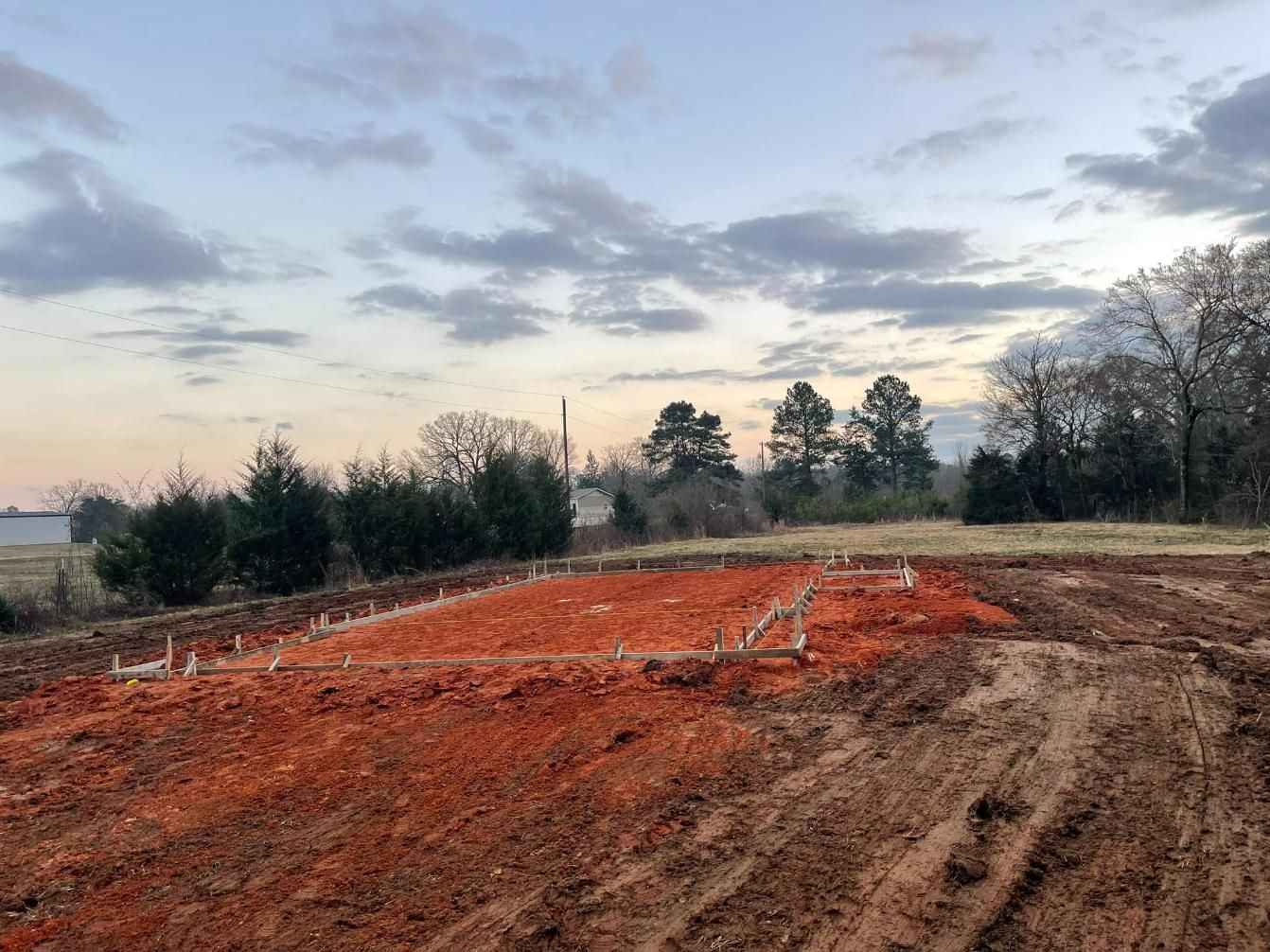 Construction site with orange dirt, foundation layout, and cloudy sky.