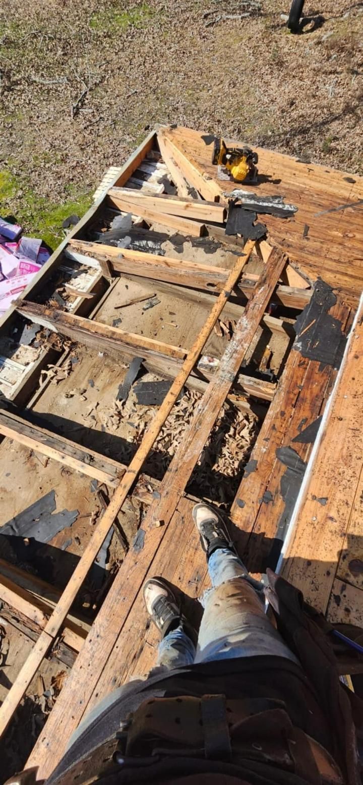Man standing on a partially dismantled roof during repairs, showing exposed joists and decking.