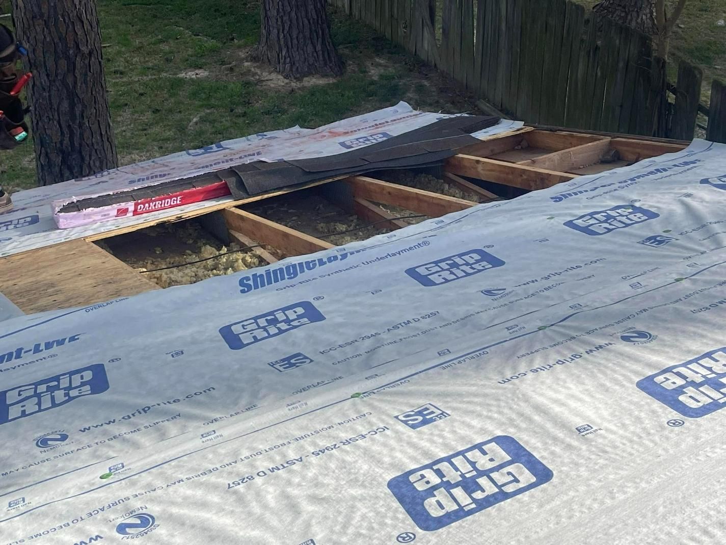 Roof under construction, covered with blue and white tarp, showing exposed wooden beams and insulation.