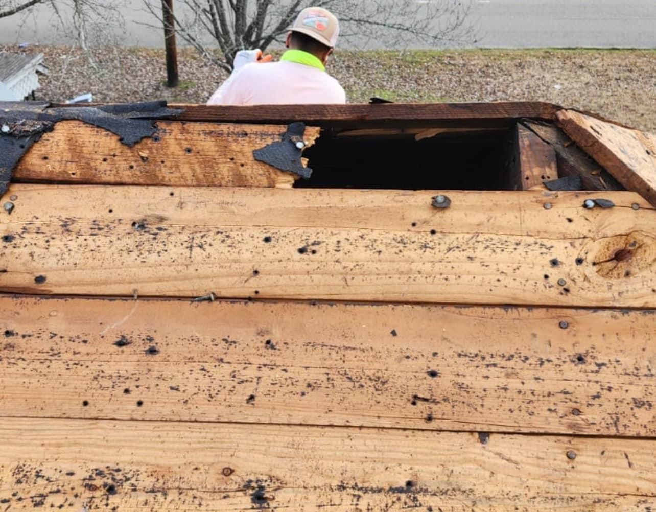 A worker in an orange hardhat inspects a wooden roof vent; sunlight illuminates weathered wood.