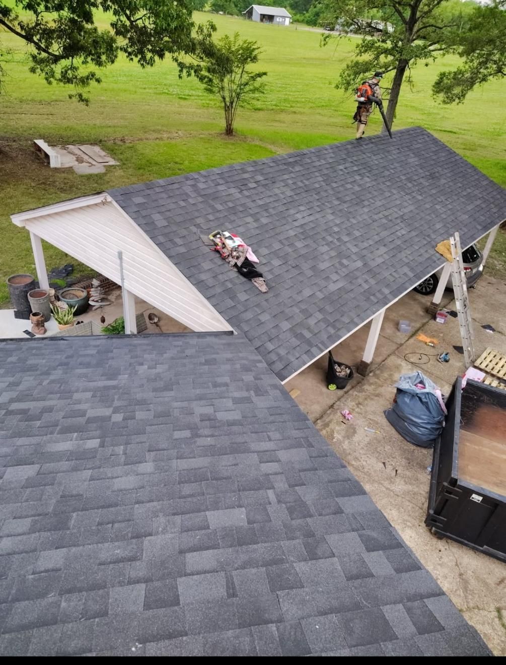 Workers on a gray shingled roof, other side white, with equipment nearby, a worker on the peak.