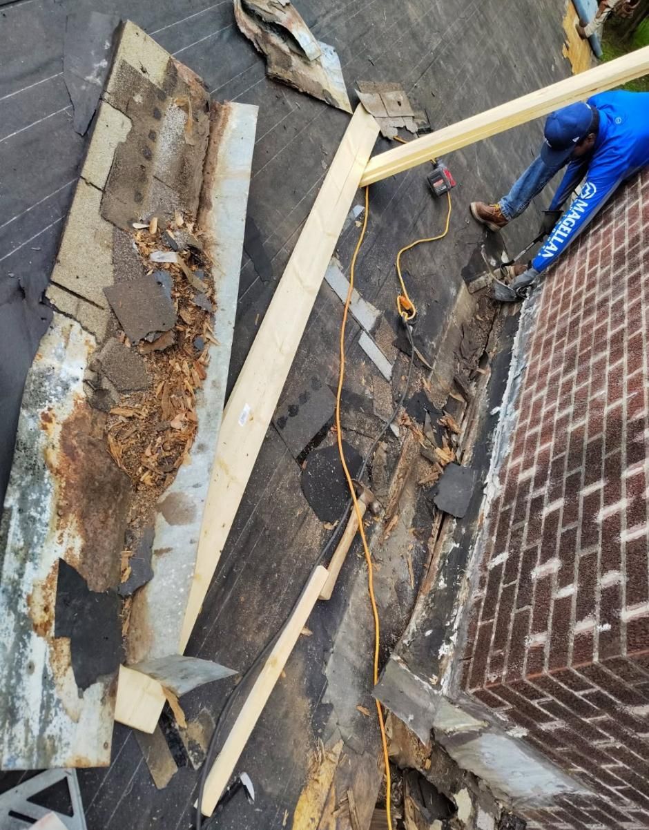 Roofer repairing damaged roof near a brick chimney; worker in blue shirt; wood debris.