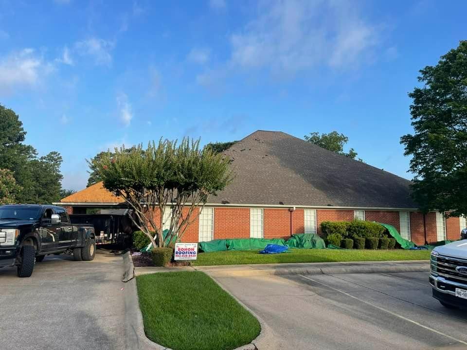 Building with new roof and red brick walls; trucks and green tarps outside.