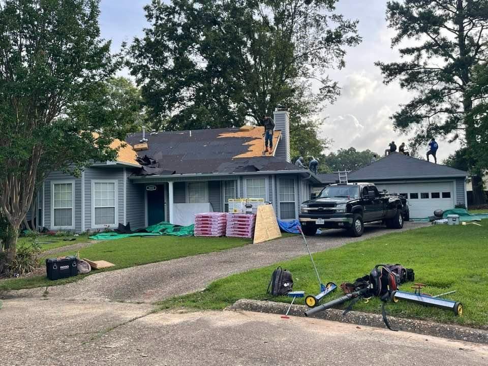 Roofers working on a house with a damaged roof, materials and truck on the lawn.