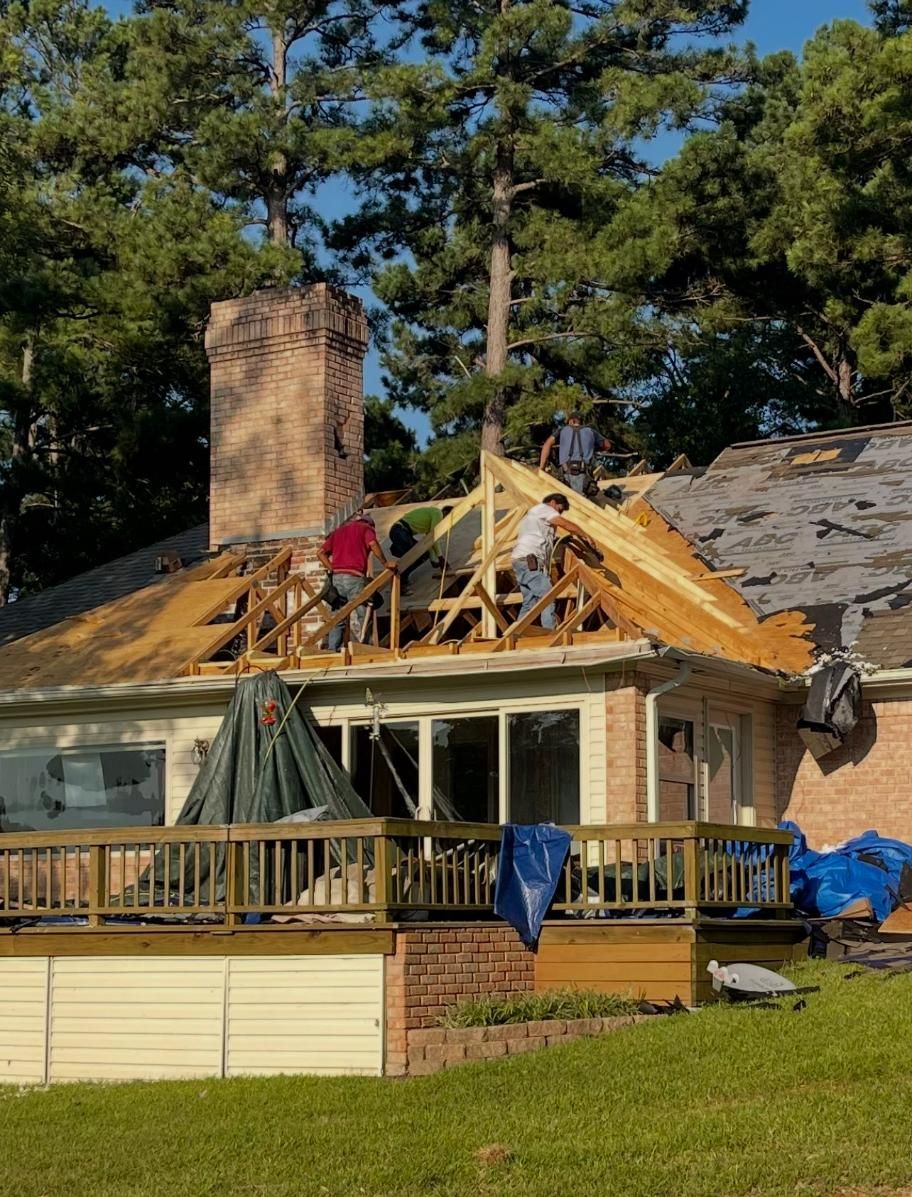 Construction workers on a roof replacing shingles, some of the old shingles still in place, on a sunny day.