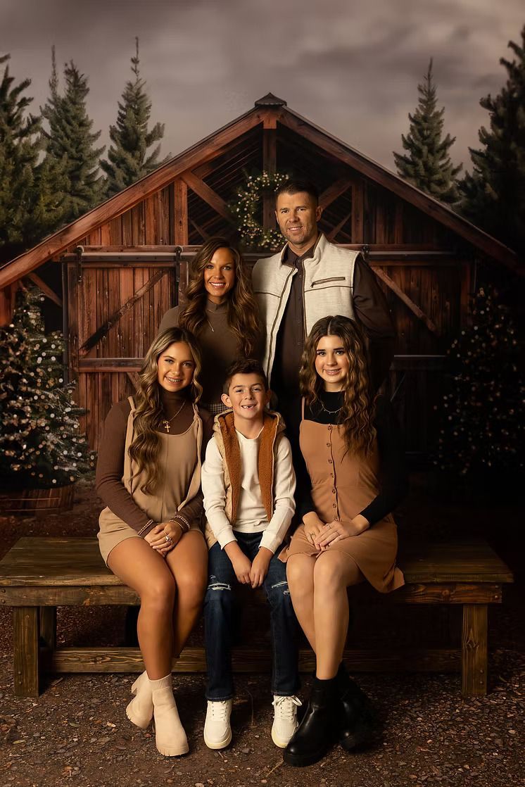 Family portrait posing in front of a wooden cabin. Brown and white outfits. People are smiling. Trees in the background.