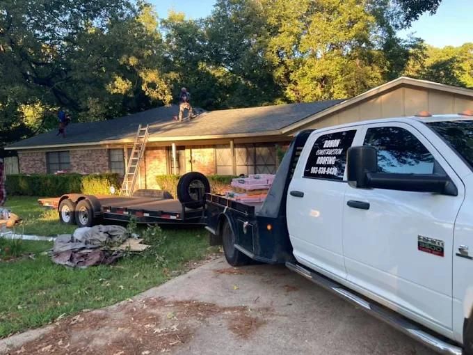 Workers on a roof, truck with trailer, ladder, removing old roof.