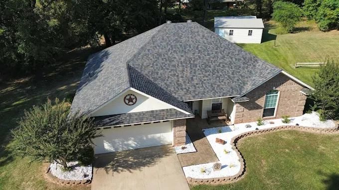Single-story brick home with gray shingle roof, white garage door, and landscaped yard.