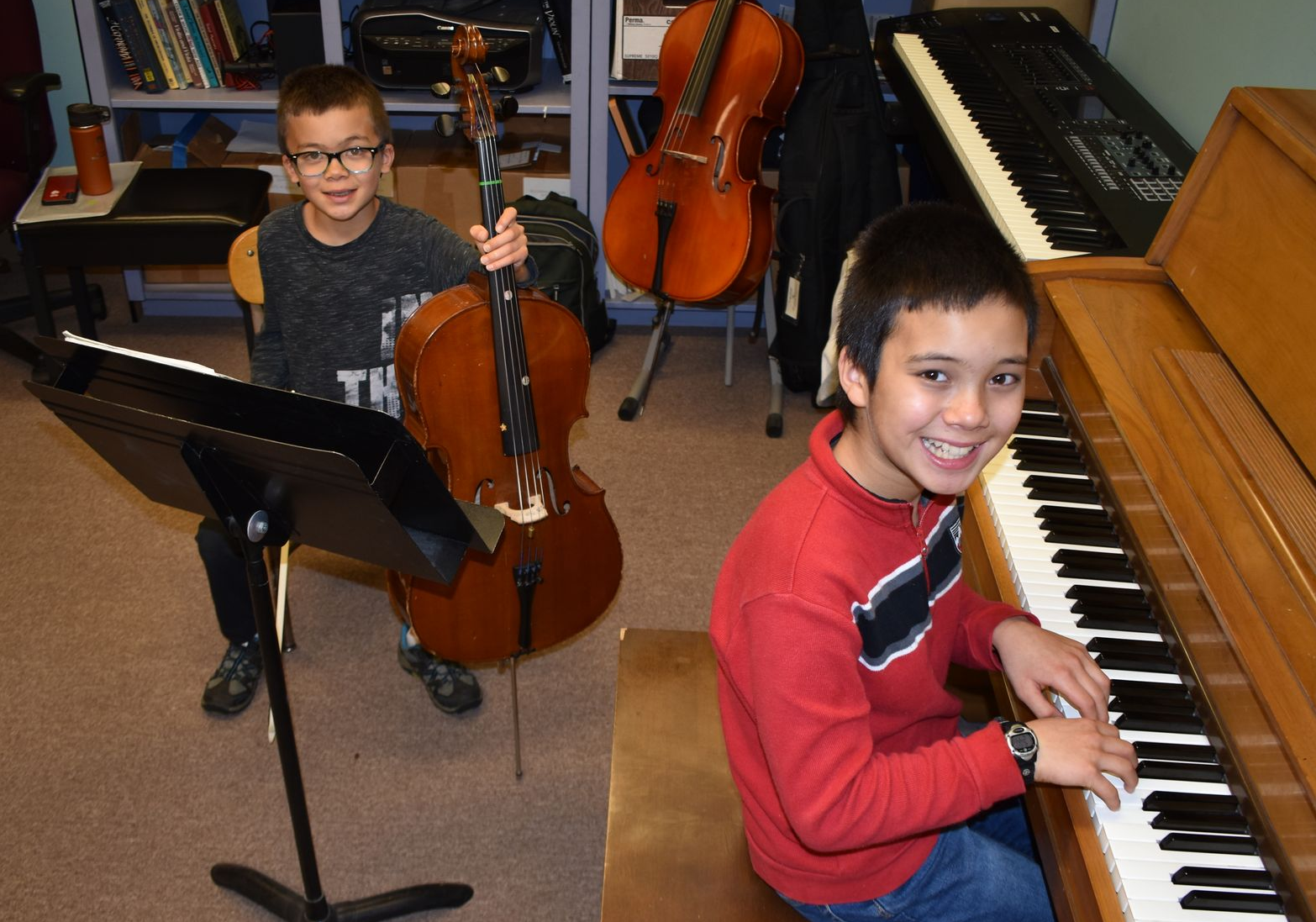 Two smiling boys, one with cello, the other at a piano.