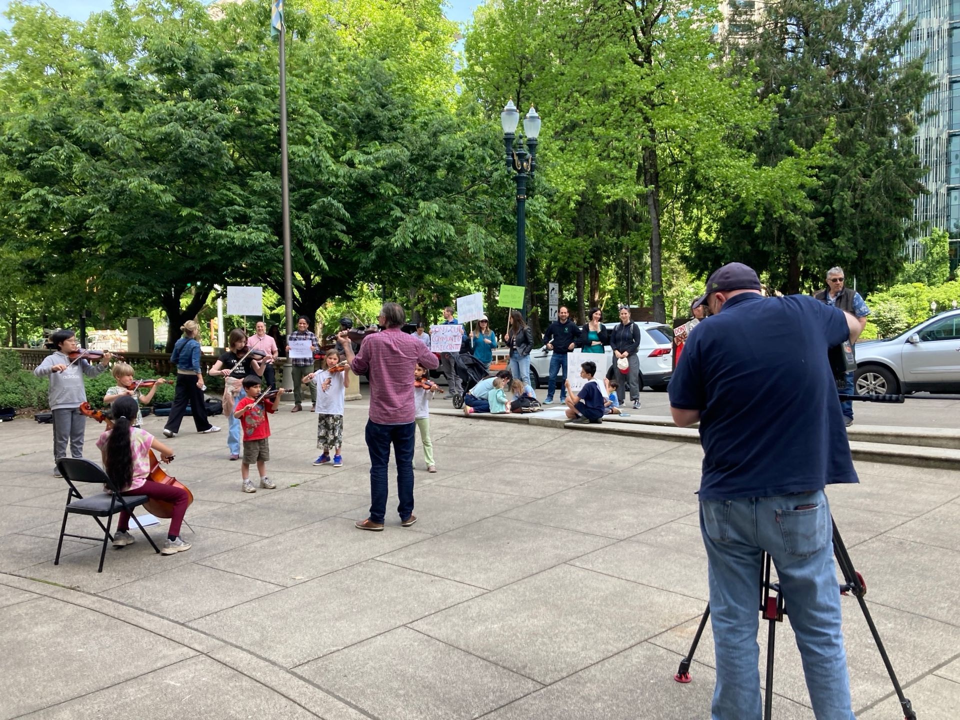 musicians and sign holders in front of City Hall, with news camera looking on
