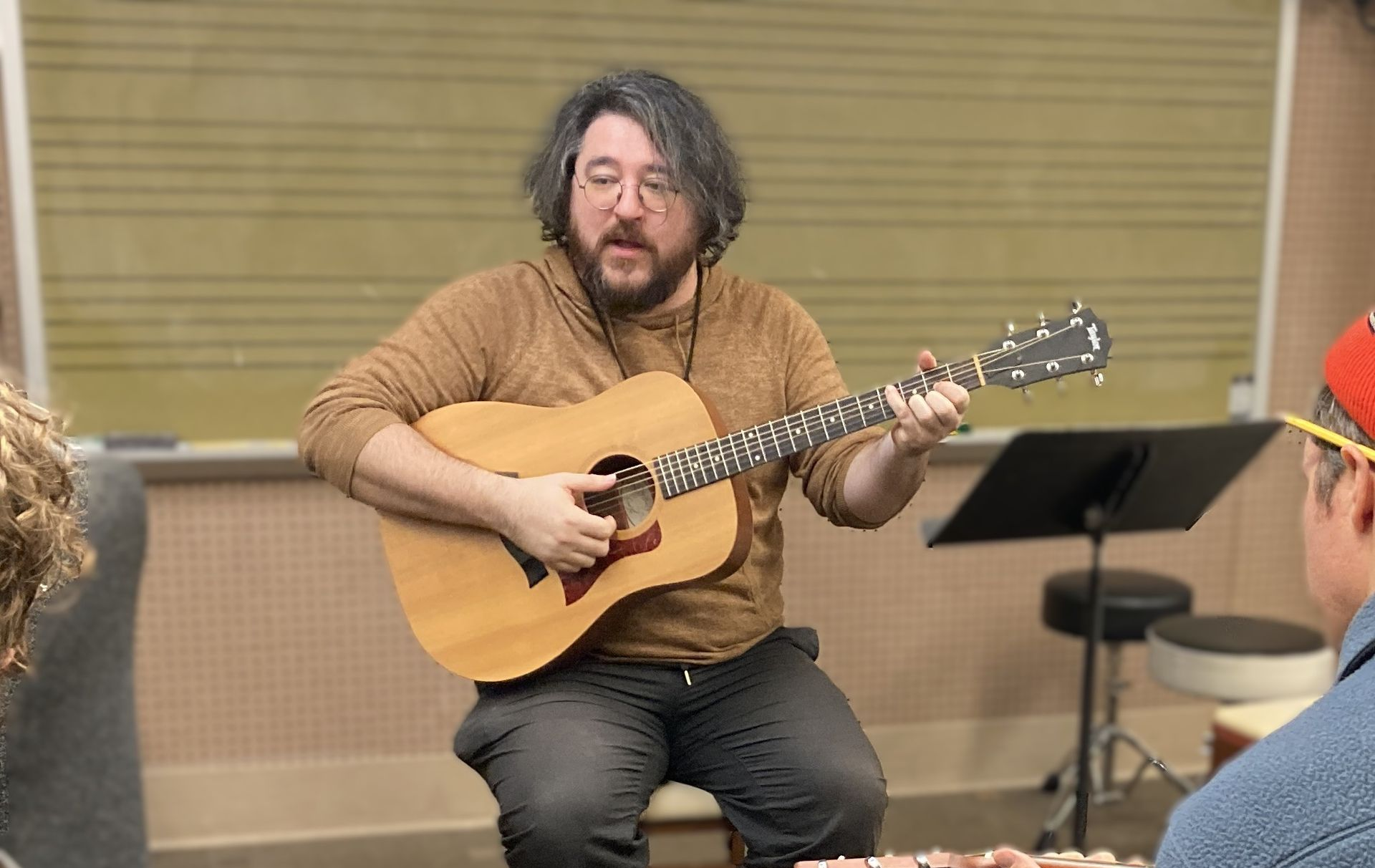 Trinh Youngman playing guitar in front of a chalkboard, with two students with guitars watching.