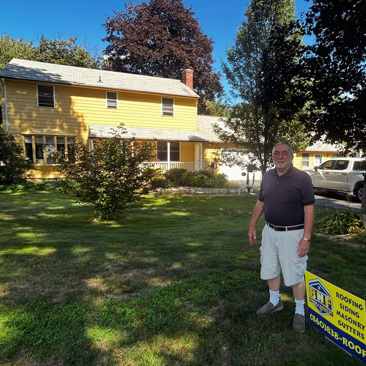 Man standing in front of yellow house with sign for roofing services.