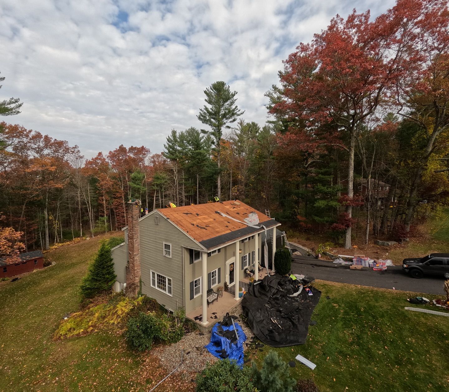 House with a partially replaced roof in a wooded area; autumn foliage.