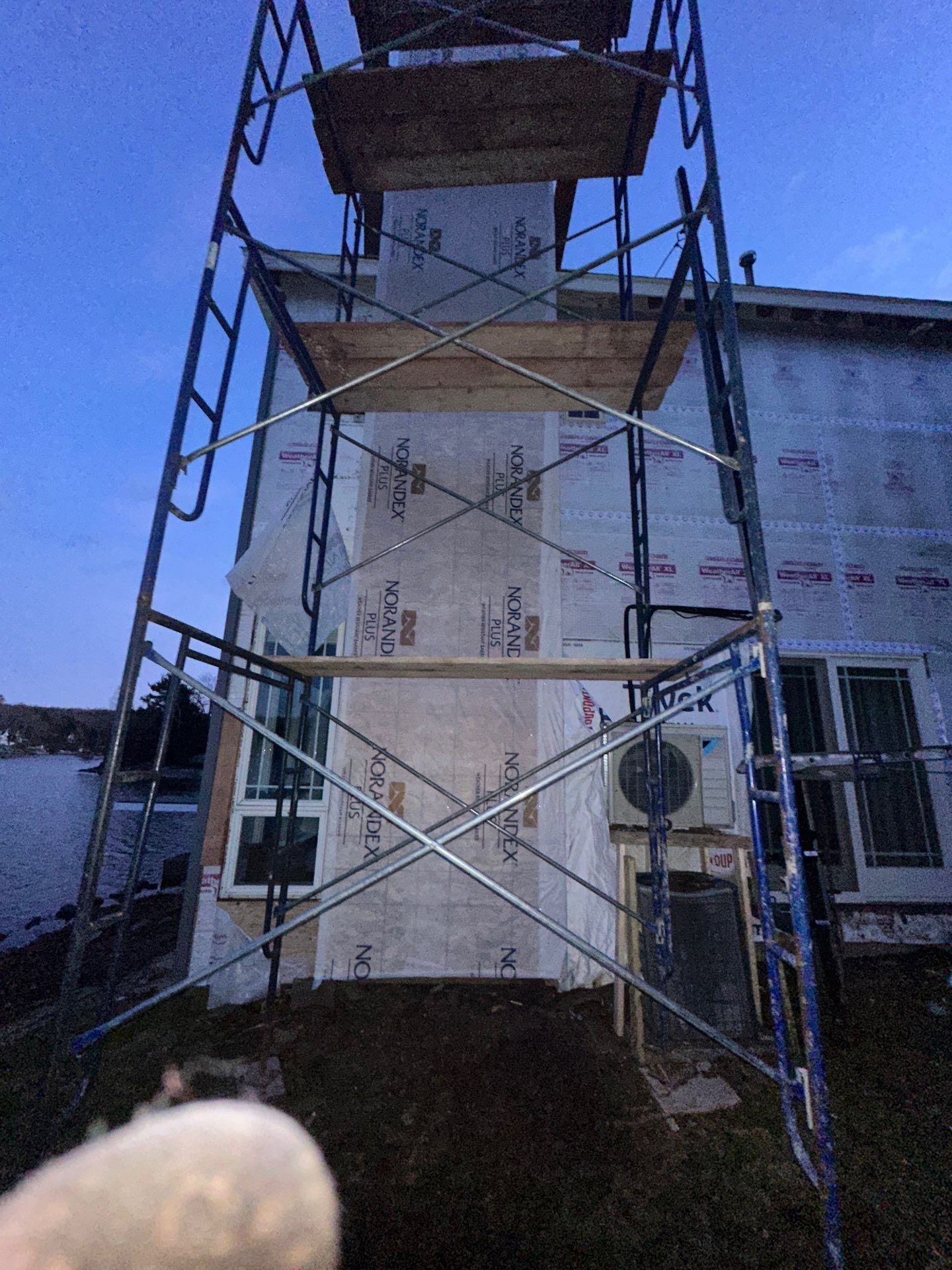 Scaffolding against a house with exposed sheathing. Evening light.