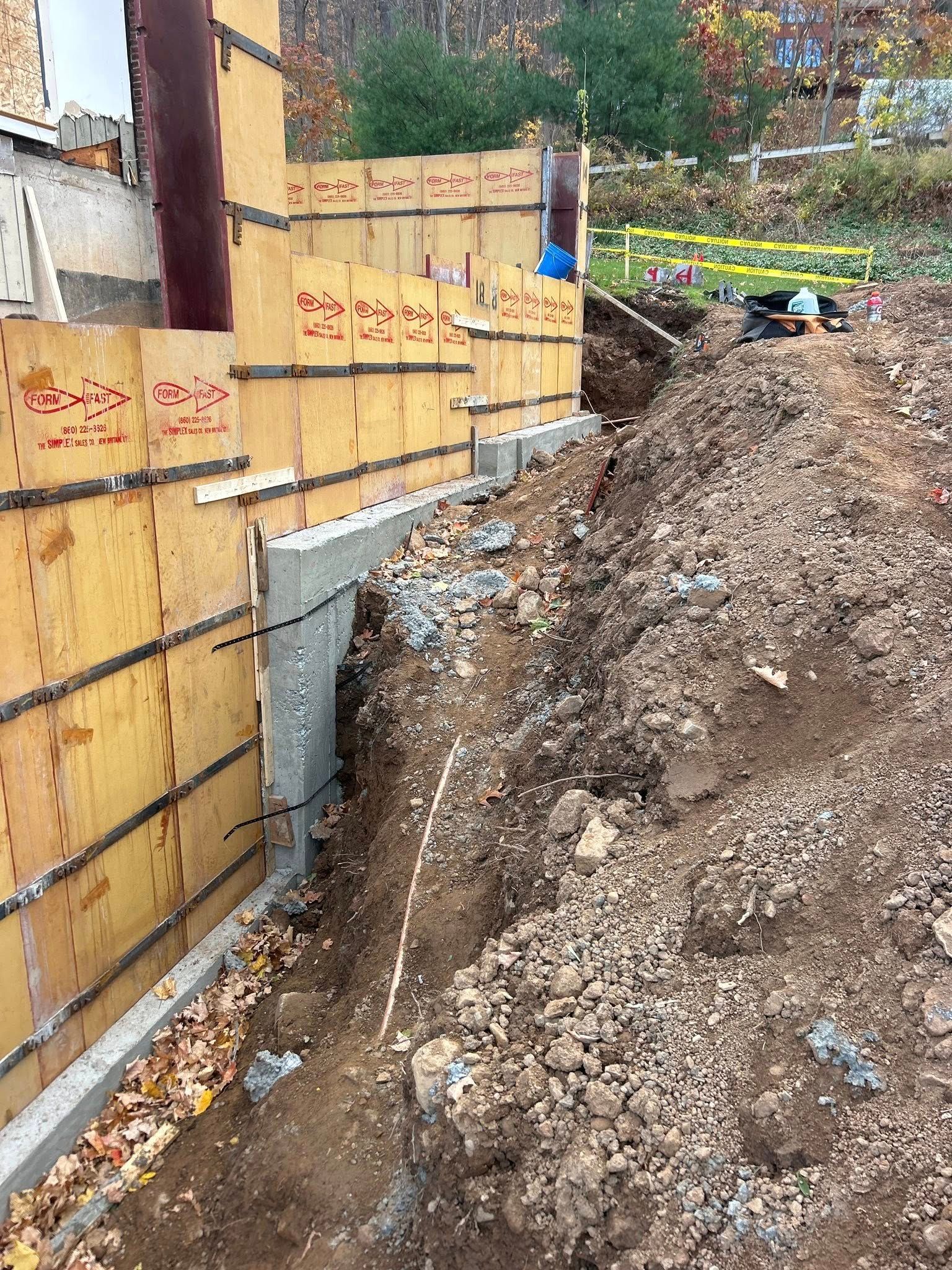 Construction site: wooden forms for a concrete wall, excavation, brown earth, fall foliage.