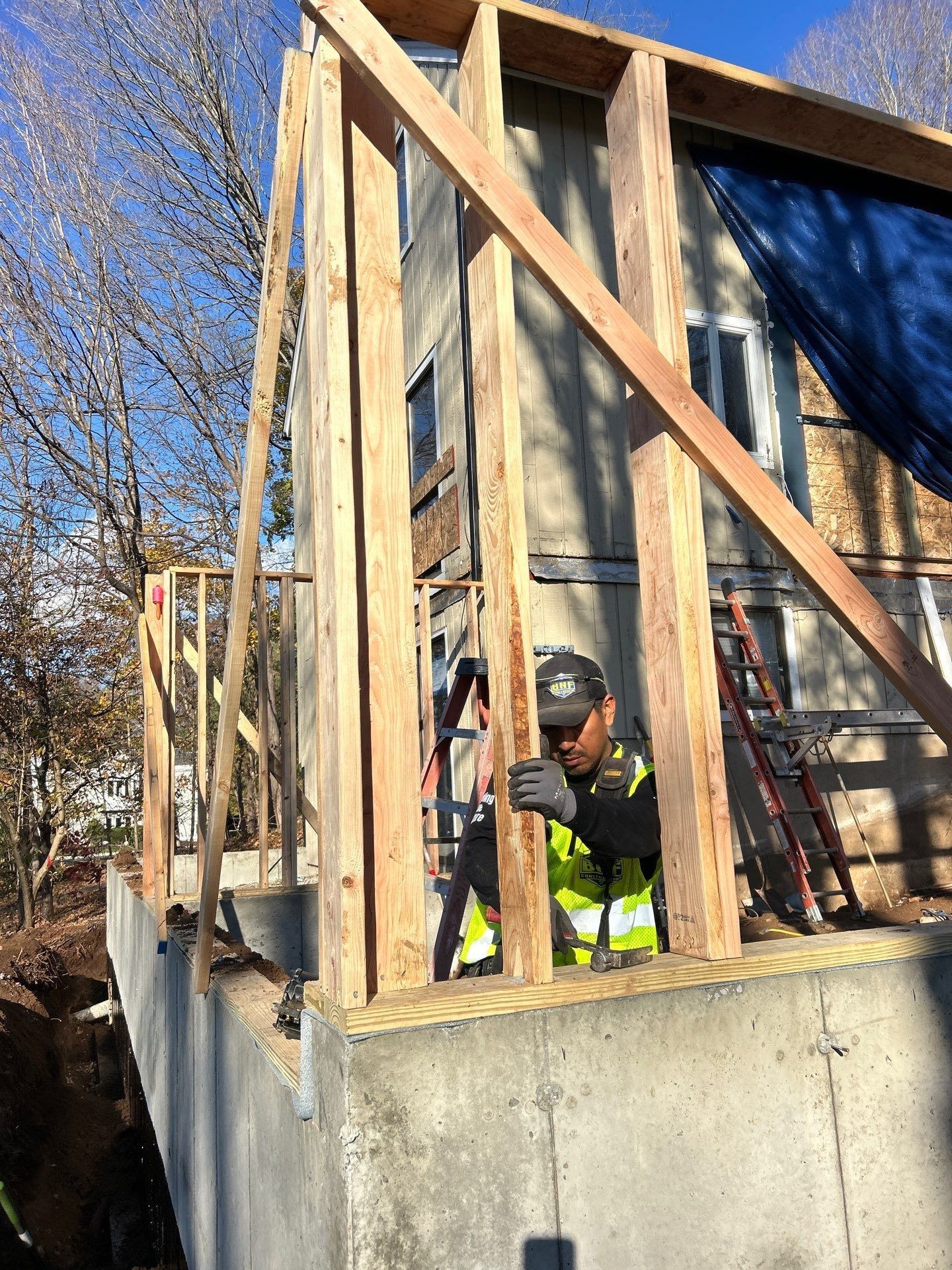 Construction worker framing a house addition, wearing a safety vest.