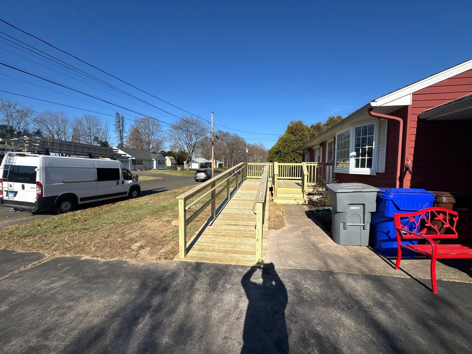 Exterior of building with accessible wooden ramp and sidewalk. White van parked on street, blue sky.