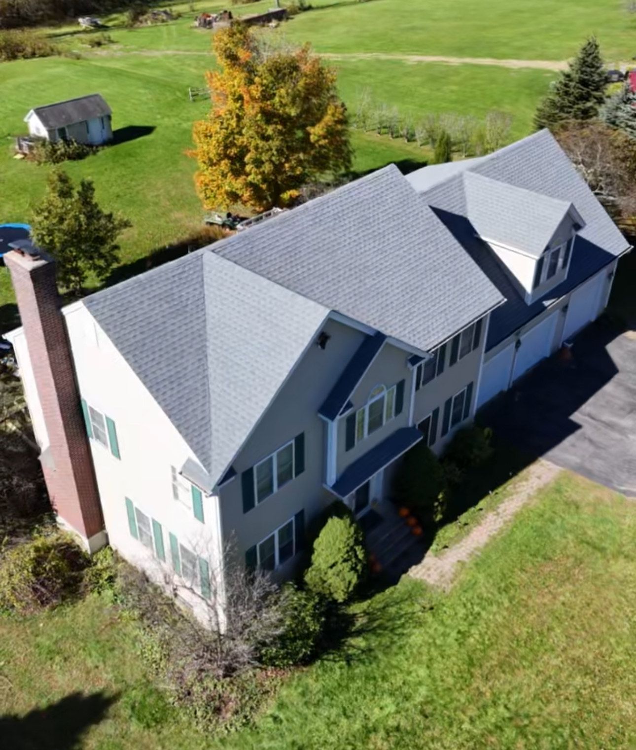 An aerial view of a two-story beige house with a gray roof and green shutters.