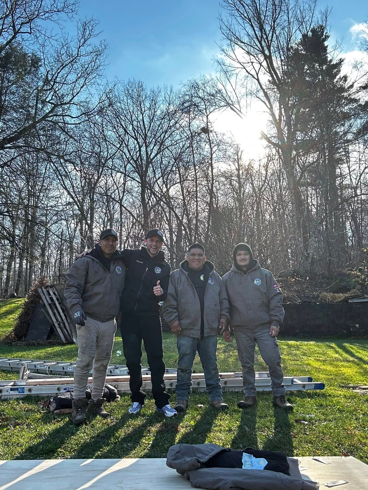 Four people in work jackets stand outside on a sunny day.