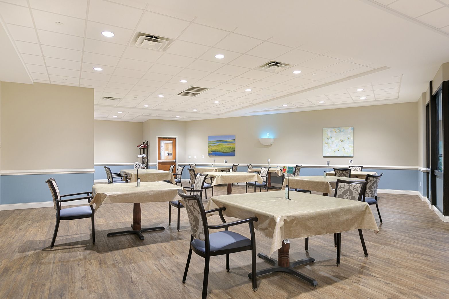 A large dining room with tables and chairs in a nursing home.
