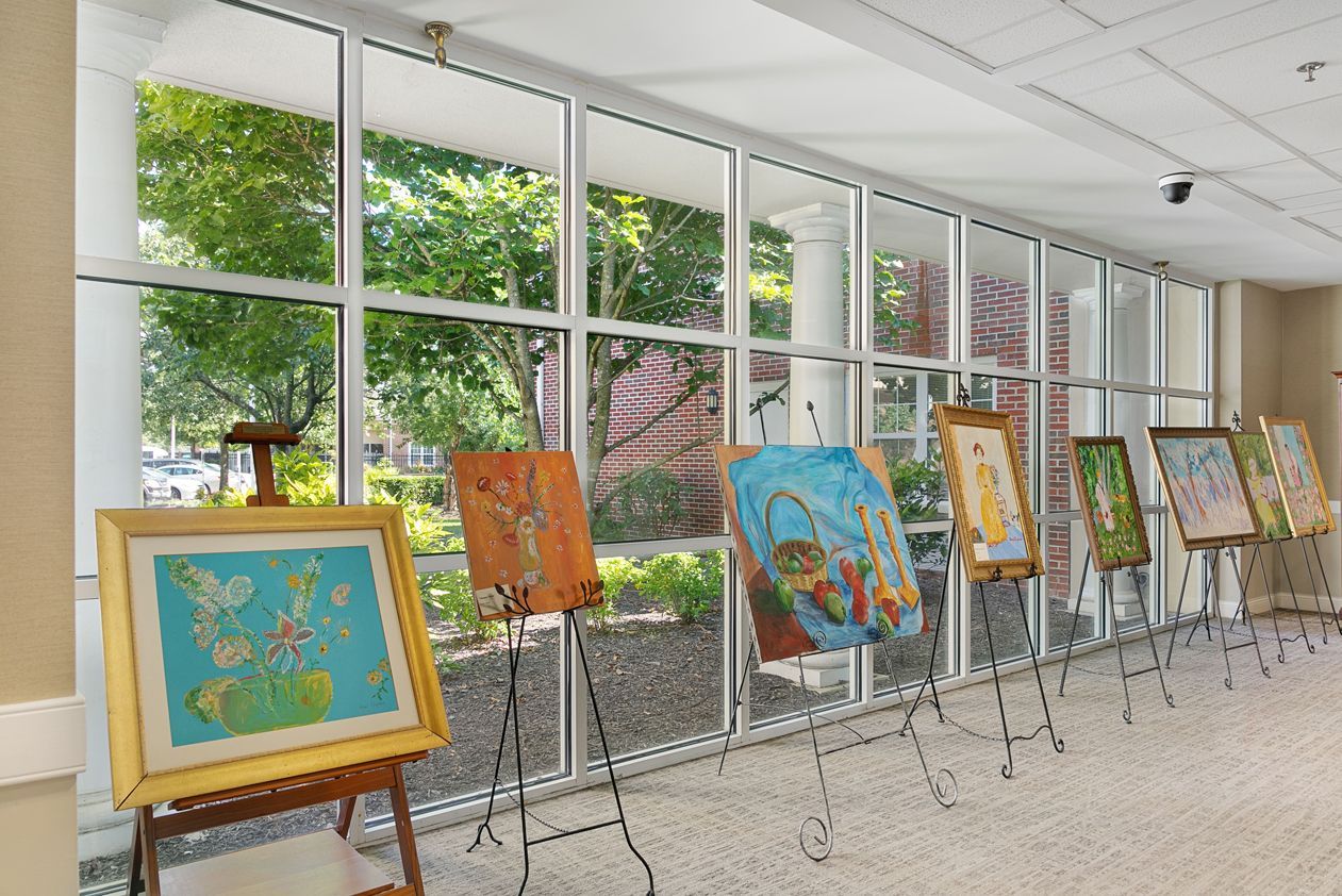 A row of paintings on easels in front of a large window.