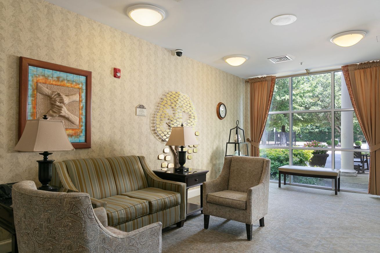 A living room with a couch , chairs , lamps and a large window.