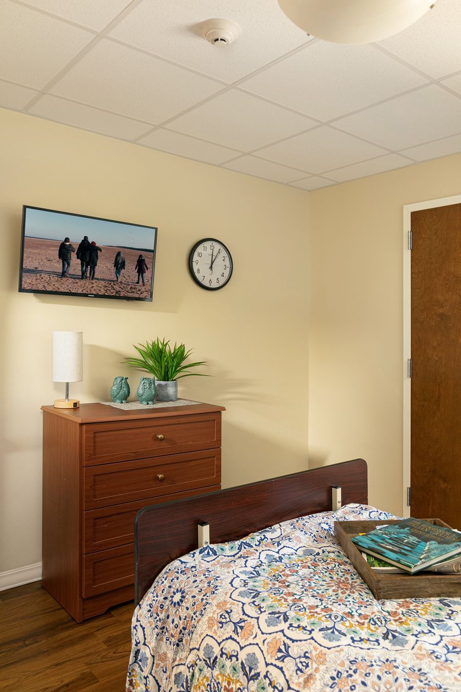 A bedroom with a bed , dresser , television and clock.