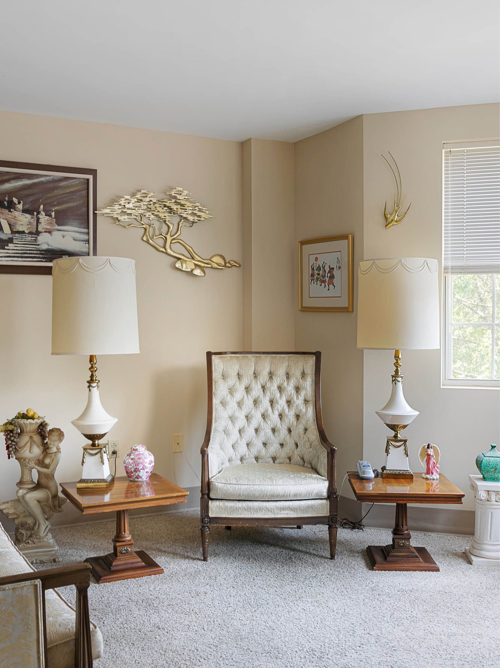 A living room with a chair , two lamps , two tables and a window.