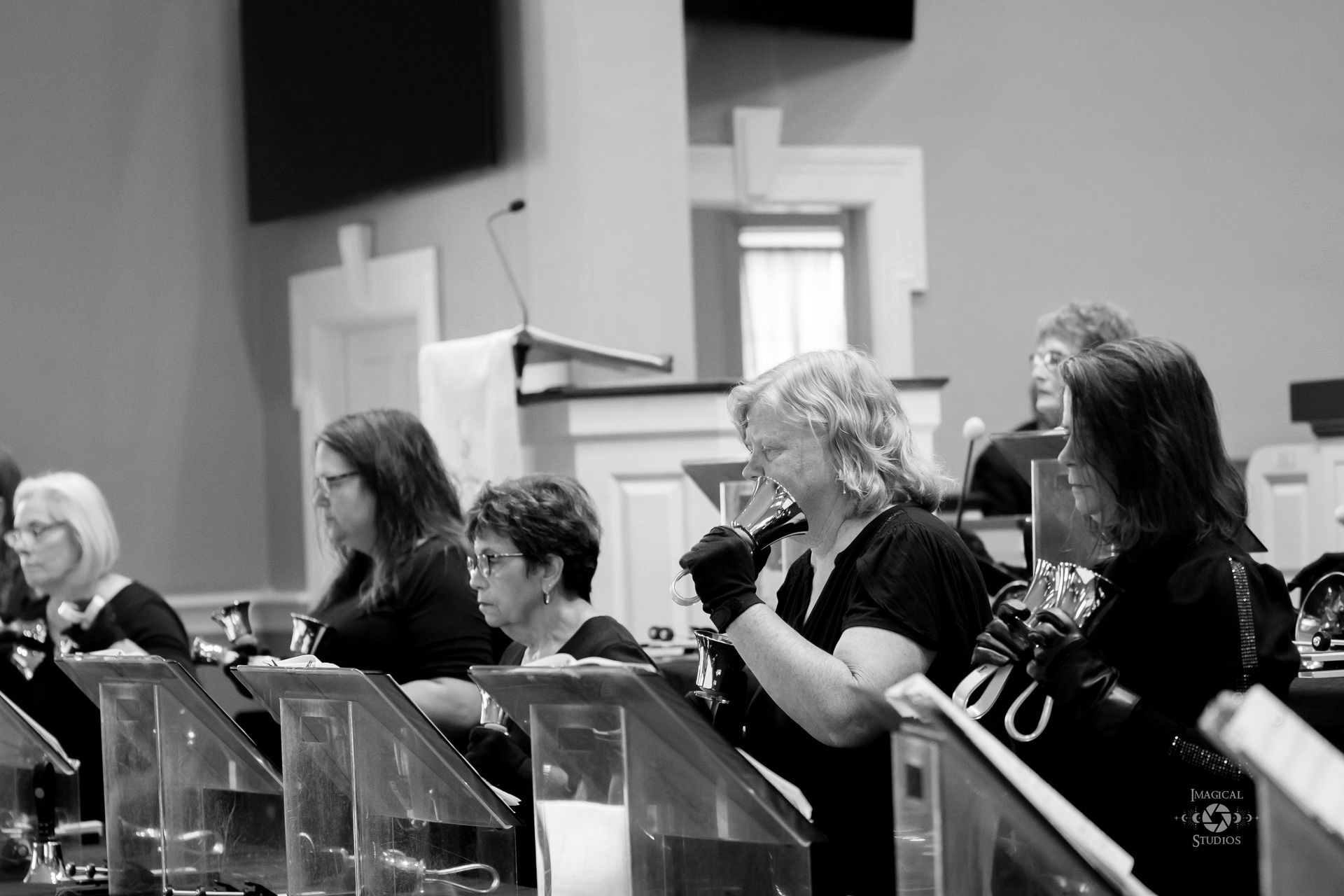 Handbell choir in a church, playing instruments. Black and white photograph.