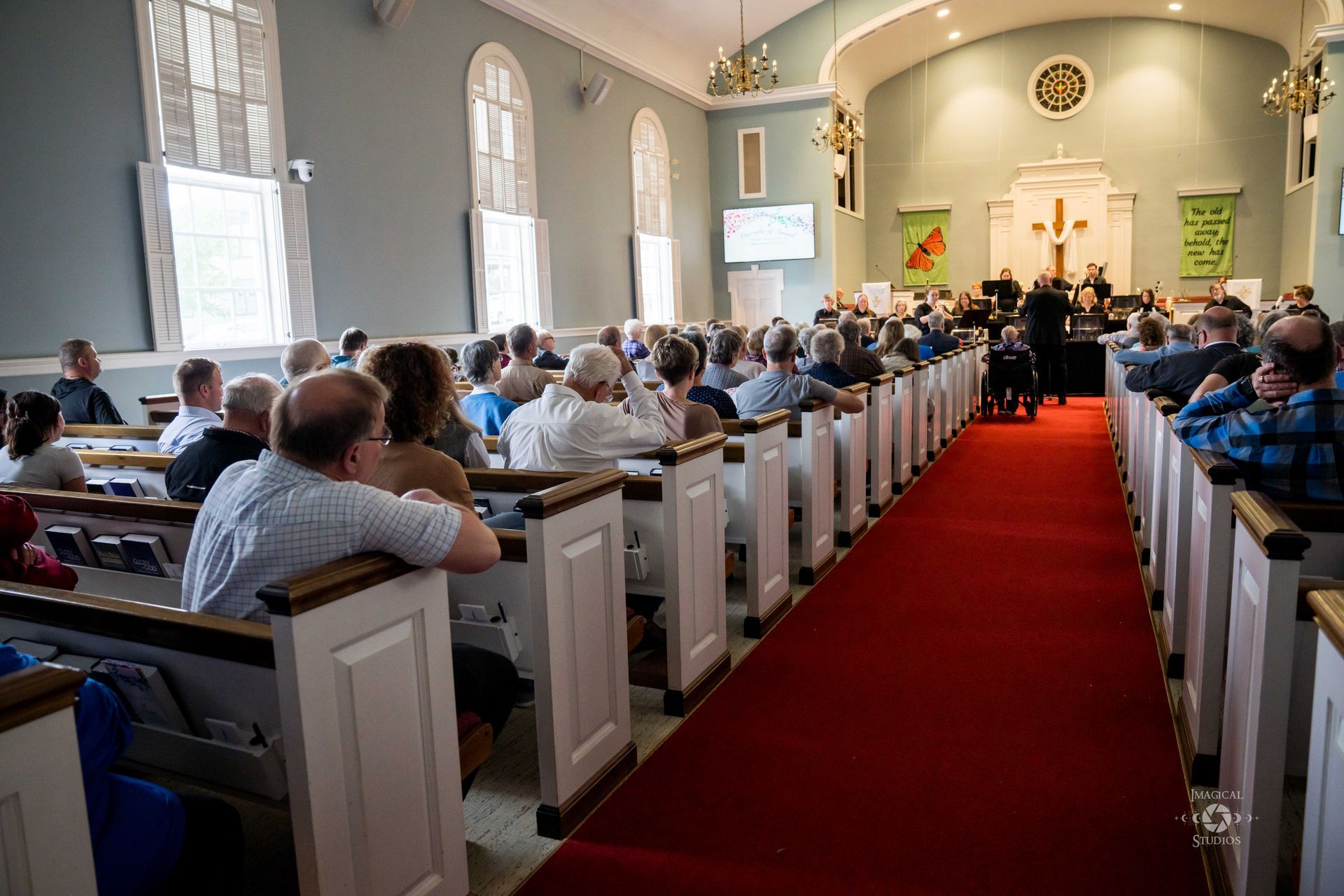 People seated in pews of a church with a red carpet aisle. A choir and band perform at the front.