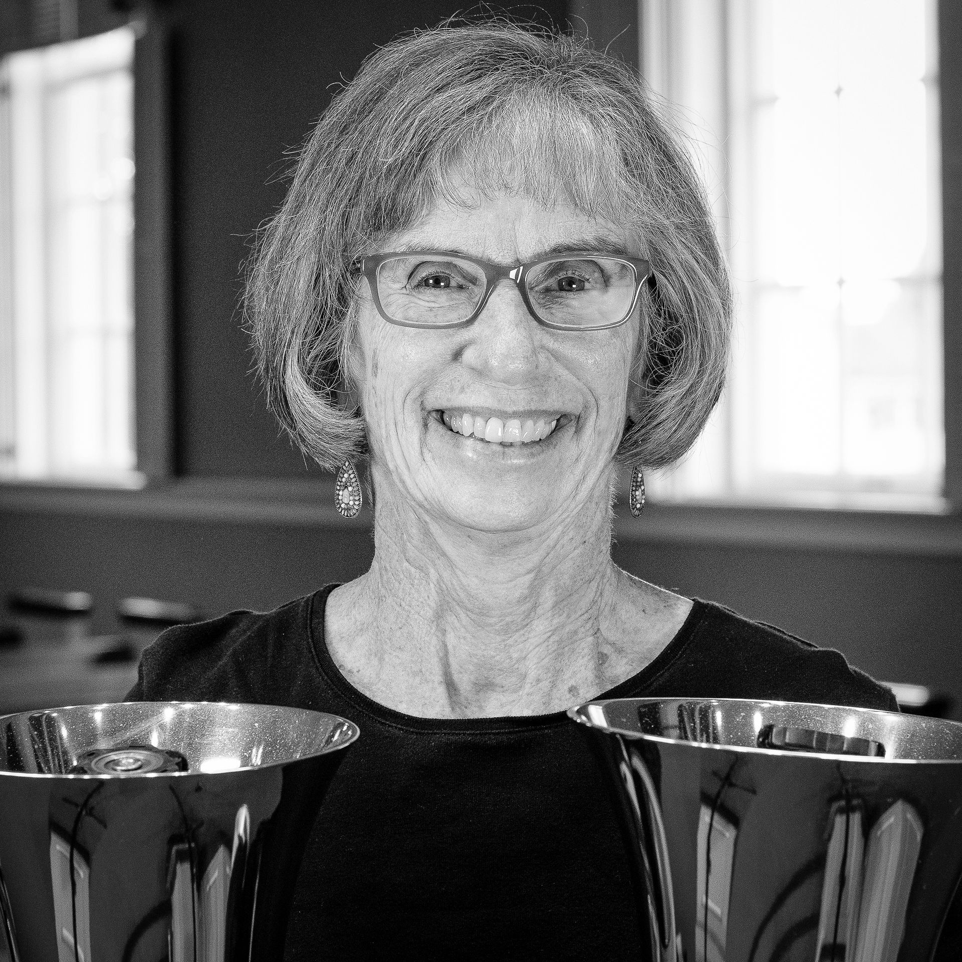Smiling woman with glasses holding two handbells.