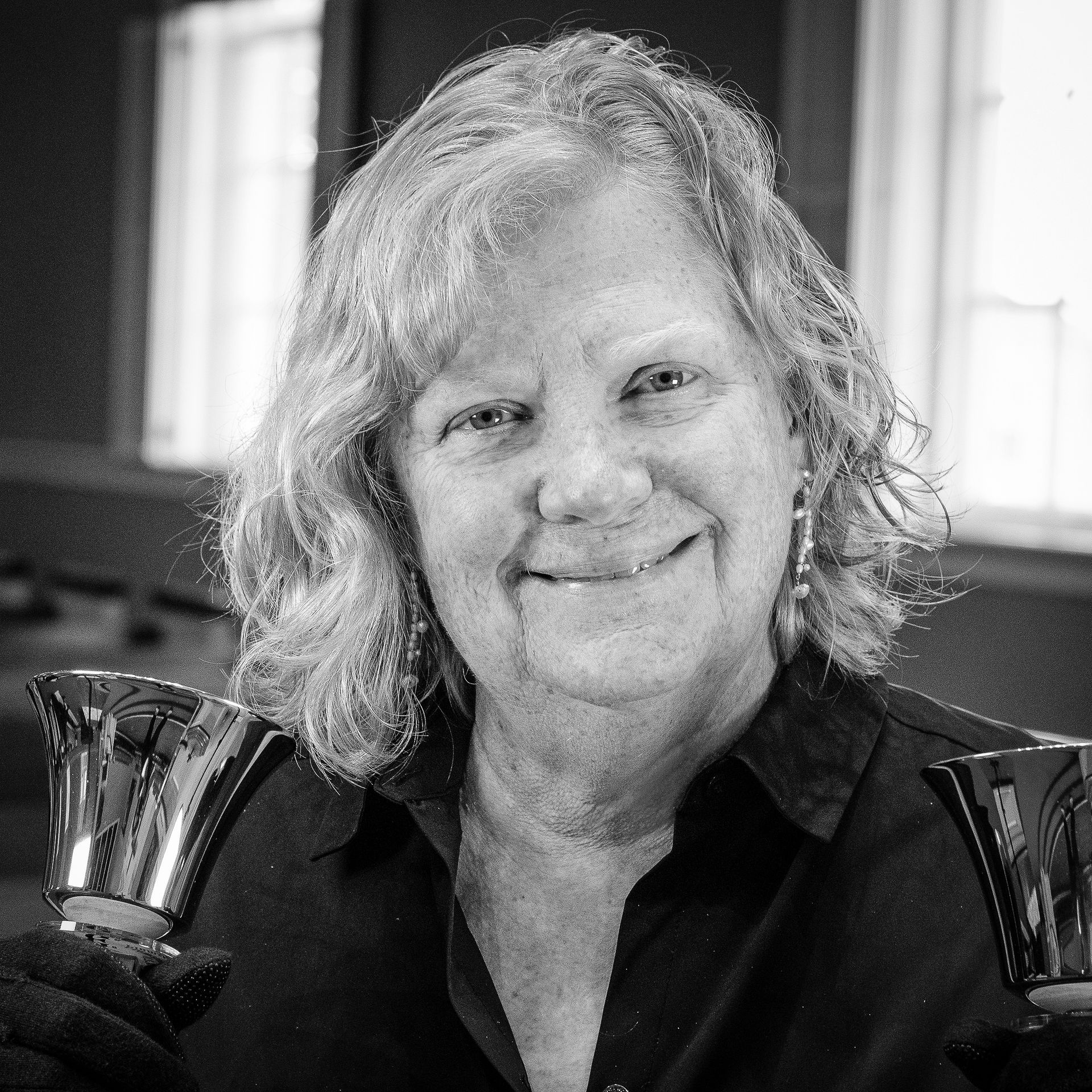 Woman holding handbells, smiling, in front of windows. Black and white photo.